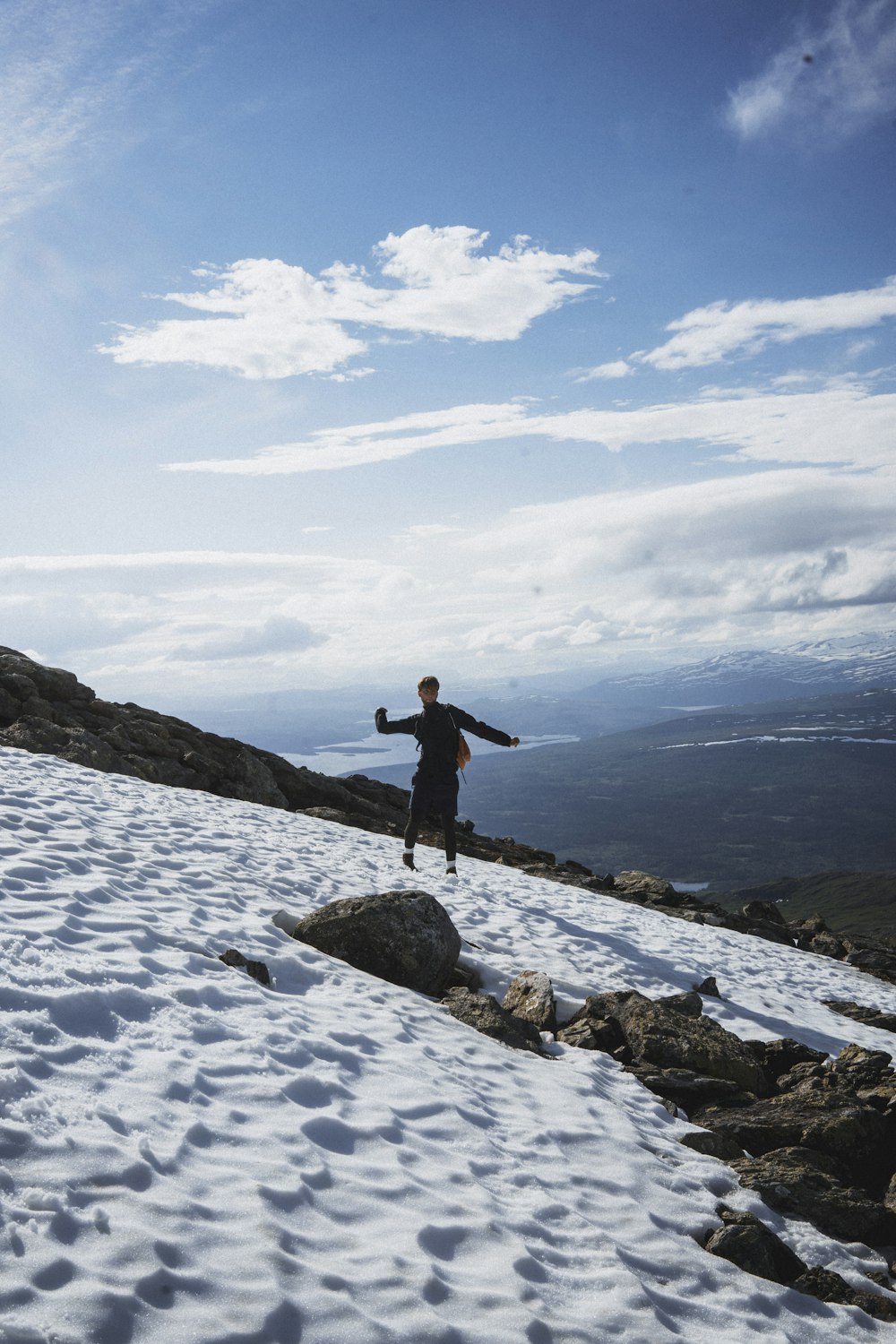 man in black jacket standing on rock formation under white clouds and blue sky during daytime