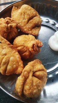 A stainless steel plate containing several crispy, golden-brown fried dumplings, accompanied by a dollop of white sauce or cream in one corner.