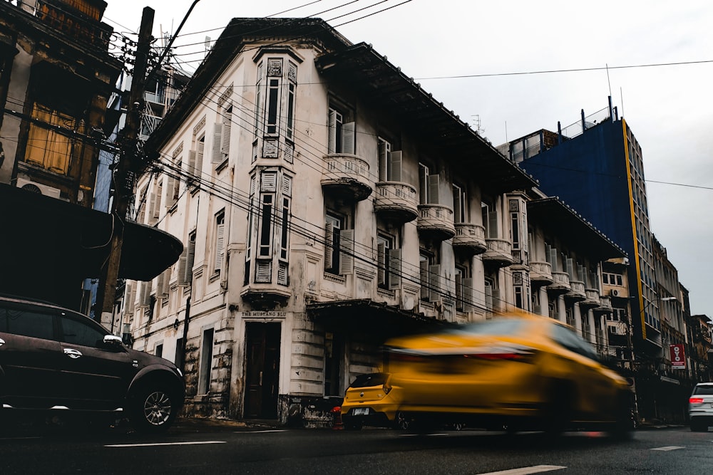 yellow car parked beside white concrete building during daytime