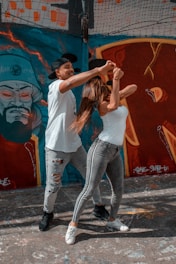 woman in white t-shirt and blue denim jeans standing beside wall with graffiti