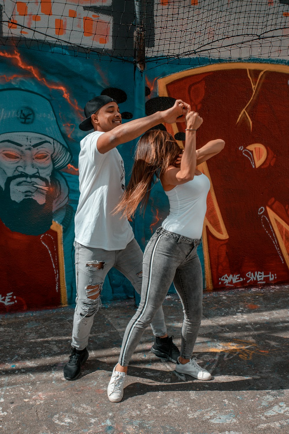 woman in white t-shirt and blue denim jeans standing beside wall with graffiti