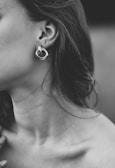 Minimalist black and white photo of a model wearing elegant, understated earrings and a necklace.