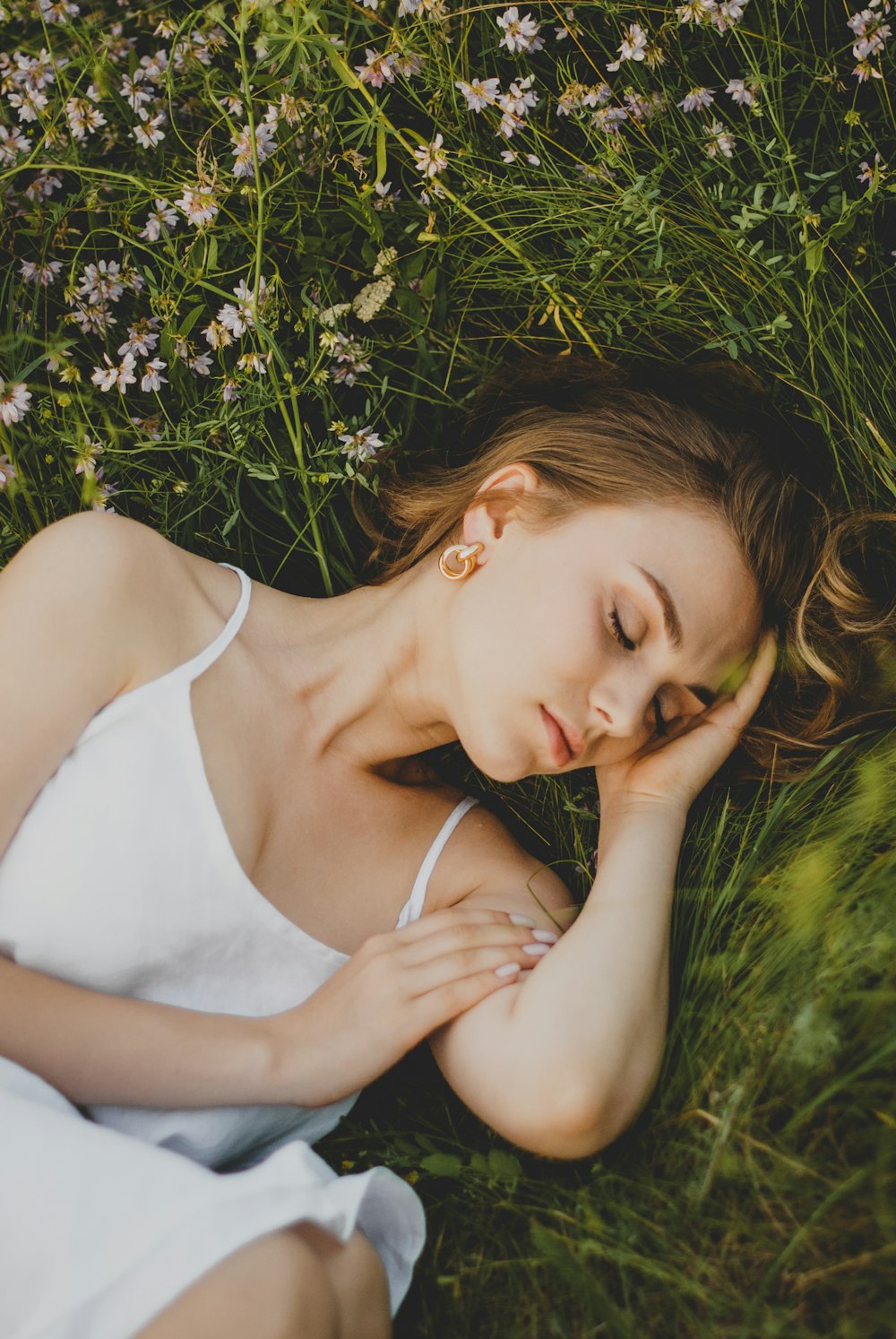 woman in white tank top lying on green grass during daytime