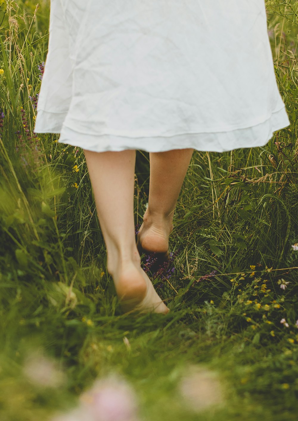 Mujer en vestido blanco de pie en el campo de hierba verde durante el día