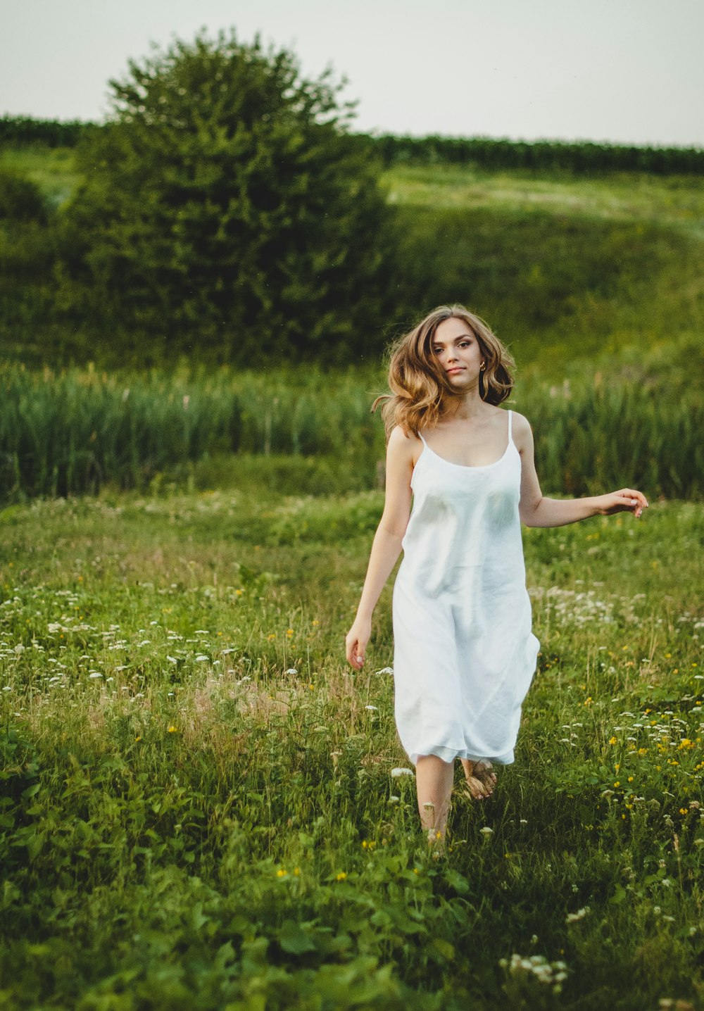 girl in white tank dress standing on green grass field during daytime