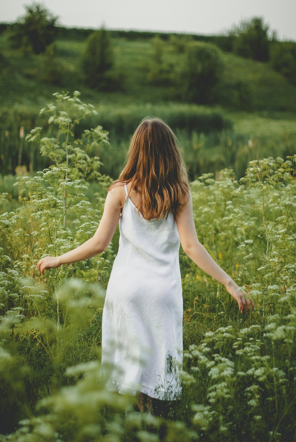 Mujer en vestido blanco sin mangas de pie en el campo de hierba verde durante el día