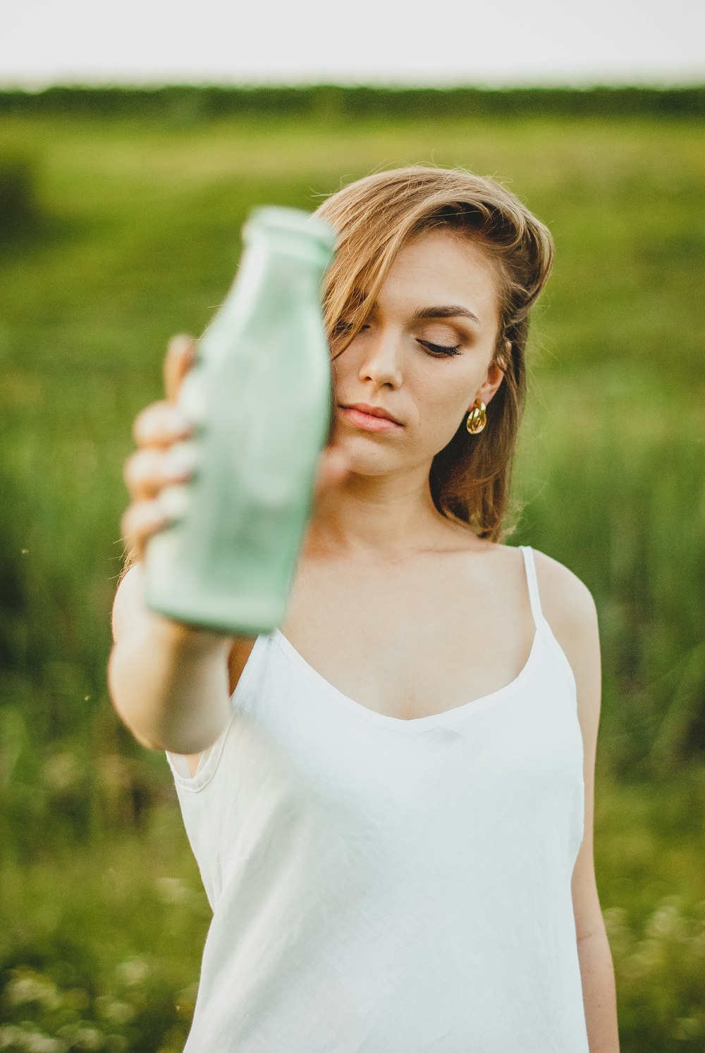 woman in white tank top holding clear glass bottle