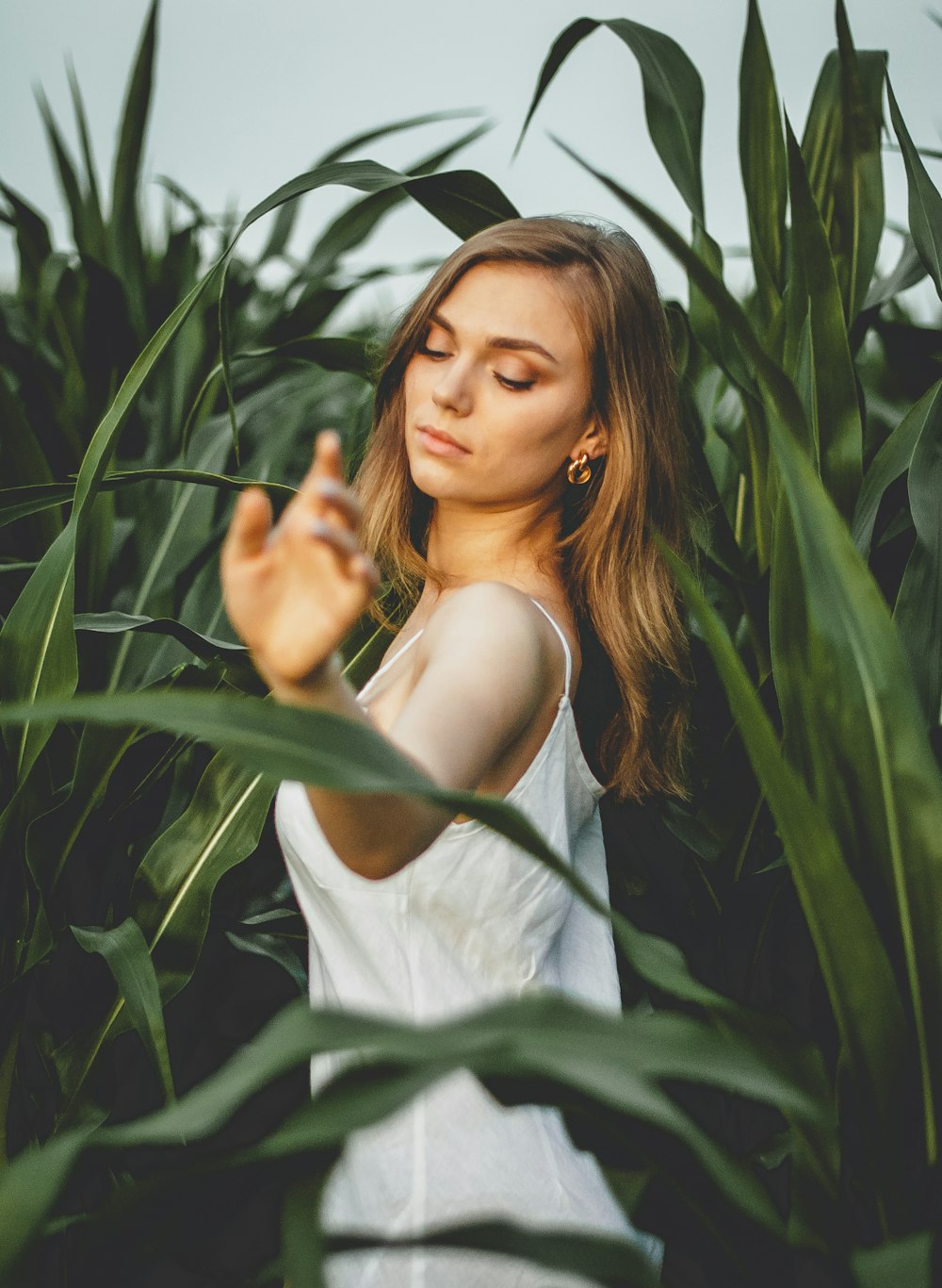 woman in white tank top standing beside green plants during daytime