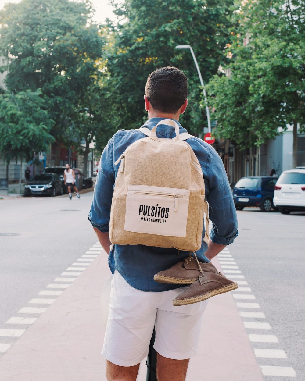 man in blue and white shirt carrying brown backpack walking on sidewalk during daytime