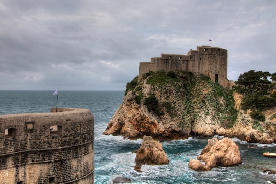 brown concrete building on cliff by the sea under white clouds during daytime in Dubrovnik Castle Croatia