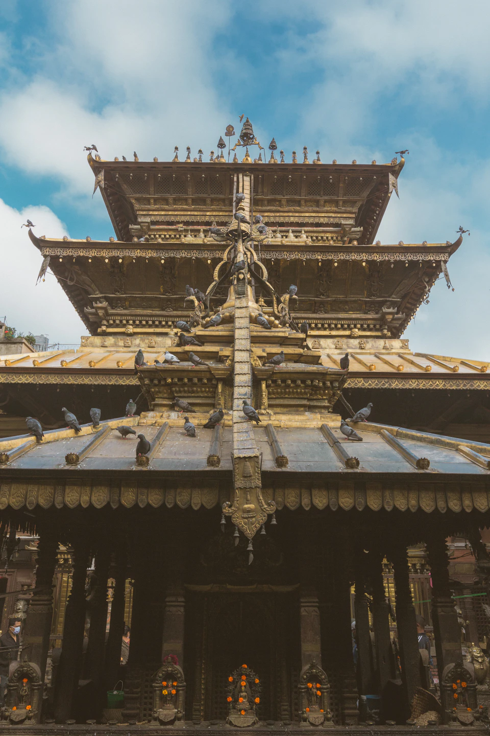 A tiered Newar pagoda temple in Patan, carved struts and a gilded roof, pigeons lining its eaves