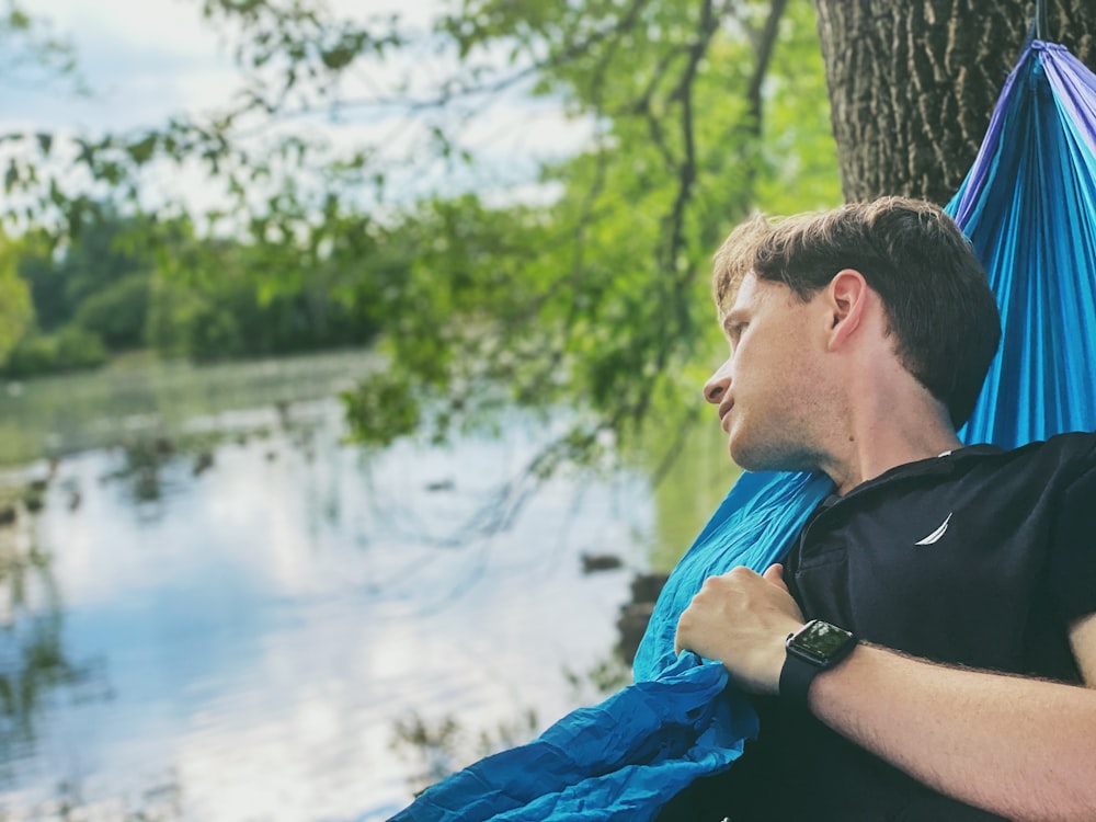 man in black shirt and blue jacket sitting on rock near body of water during daytime