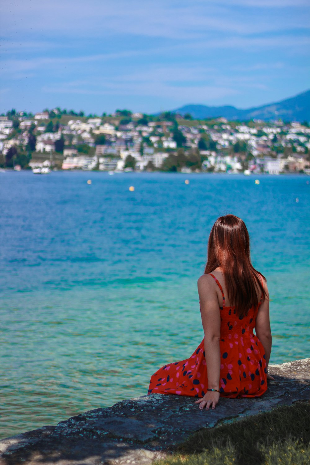 woman in red and black floral dress standing near body of water during daytime