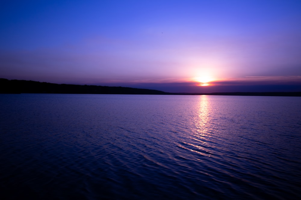 mar calmo sob o céu azul durante o pôr do sol