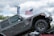 A gray Jeep Rubicon is positioned on an inclined ramp, demonstrating its off-road capabilities. In the background, a large American flag waves against a cloudy sky. There are banners advertising a lifetime limited warranty, and tree foliage is visible, suggesting an outdoor setting.