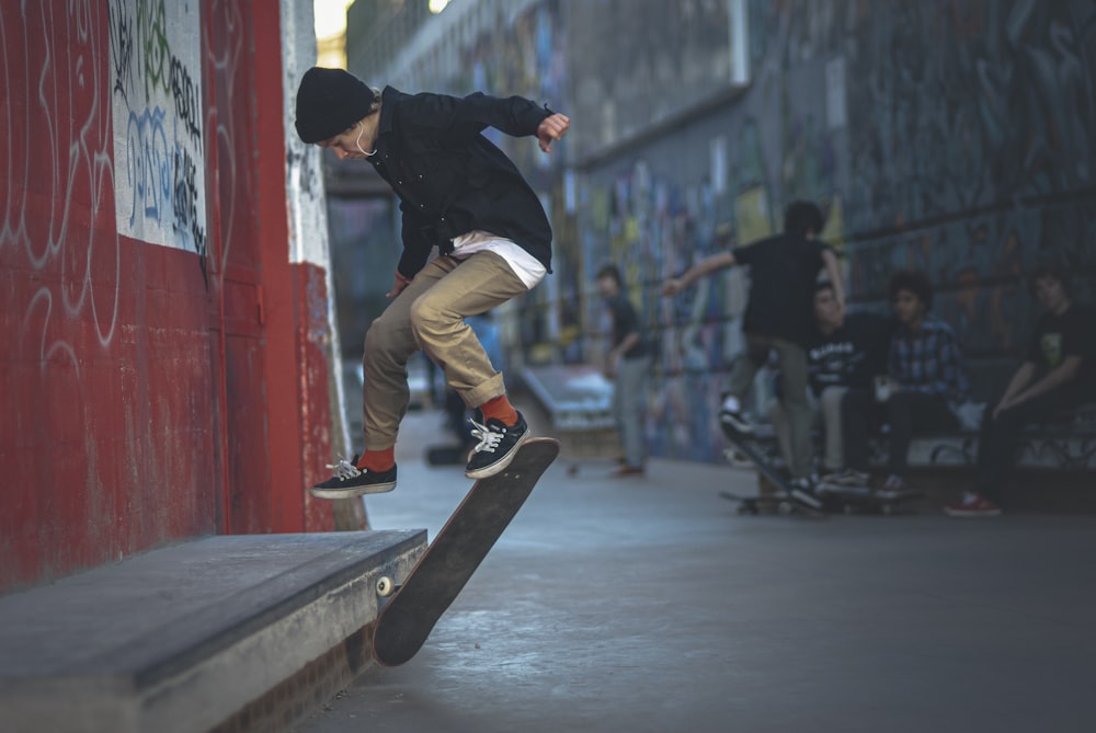 homme en veste noire et pantalon faire des cascades de skateboard