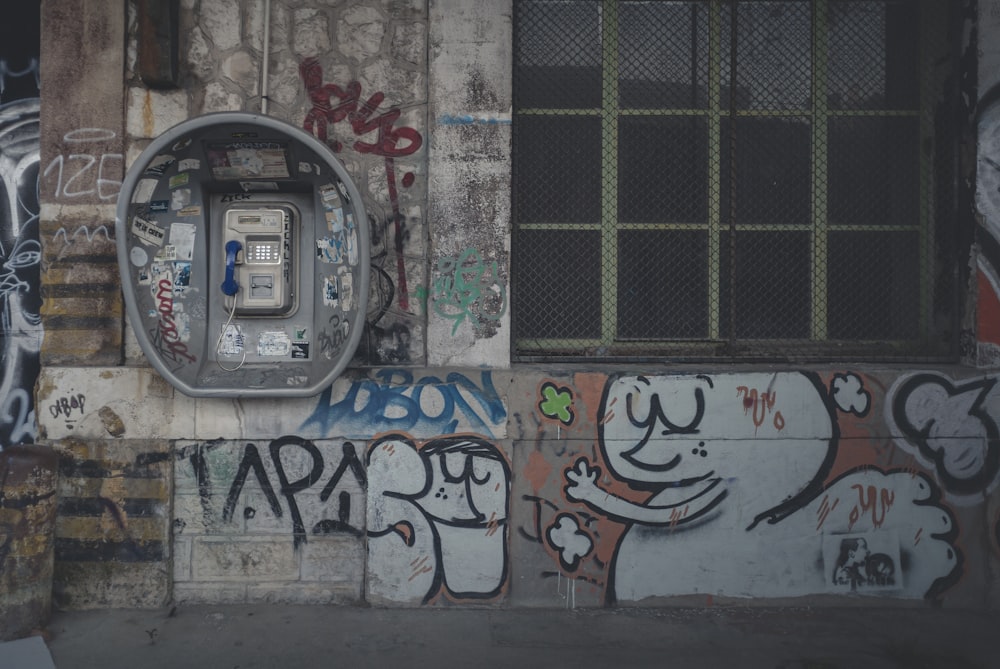 落書きのある白い壁の横の灰色の電話ボックス