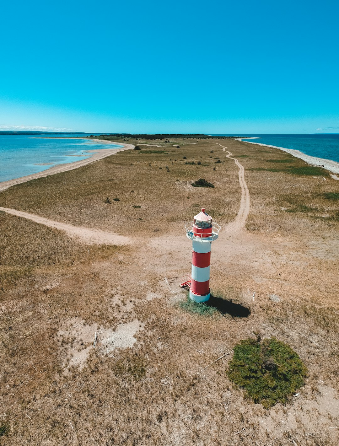 white and red lighthouse on brown sand near blue sea under blue sky during daytime