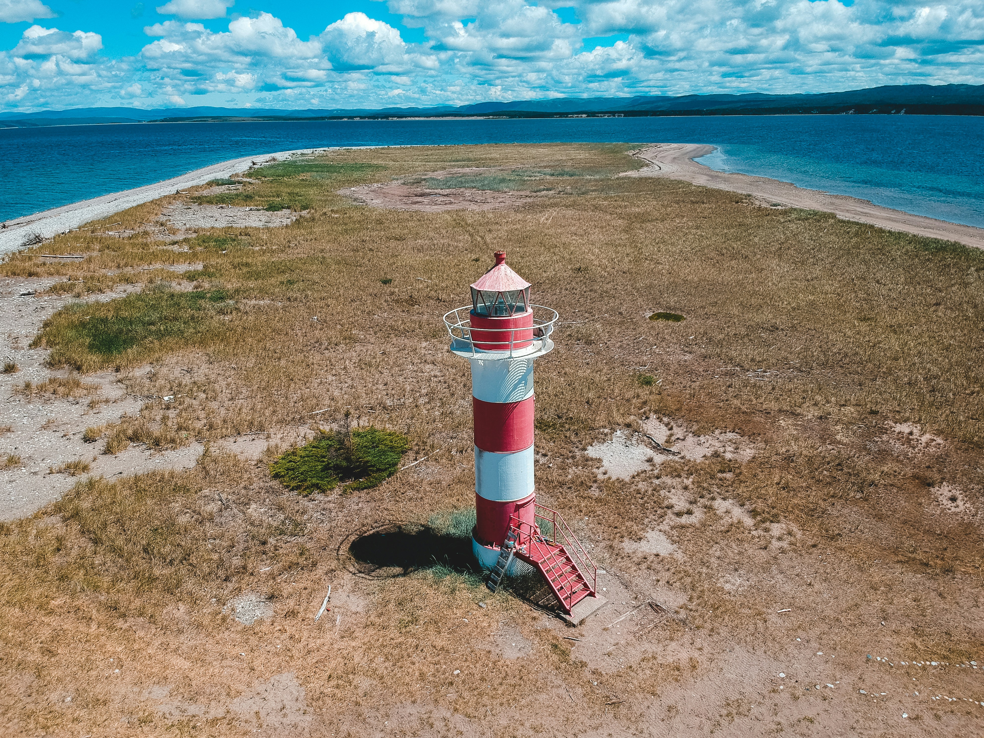 White and red lighthouse on brown sand near body of water during ...