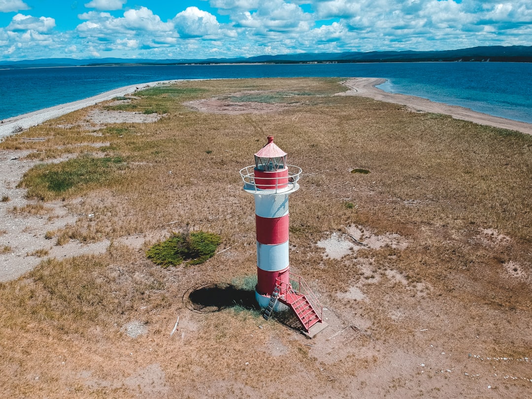 white and red lighthouse on brown sand near body of water during daytime