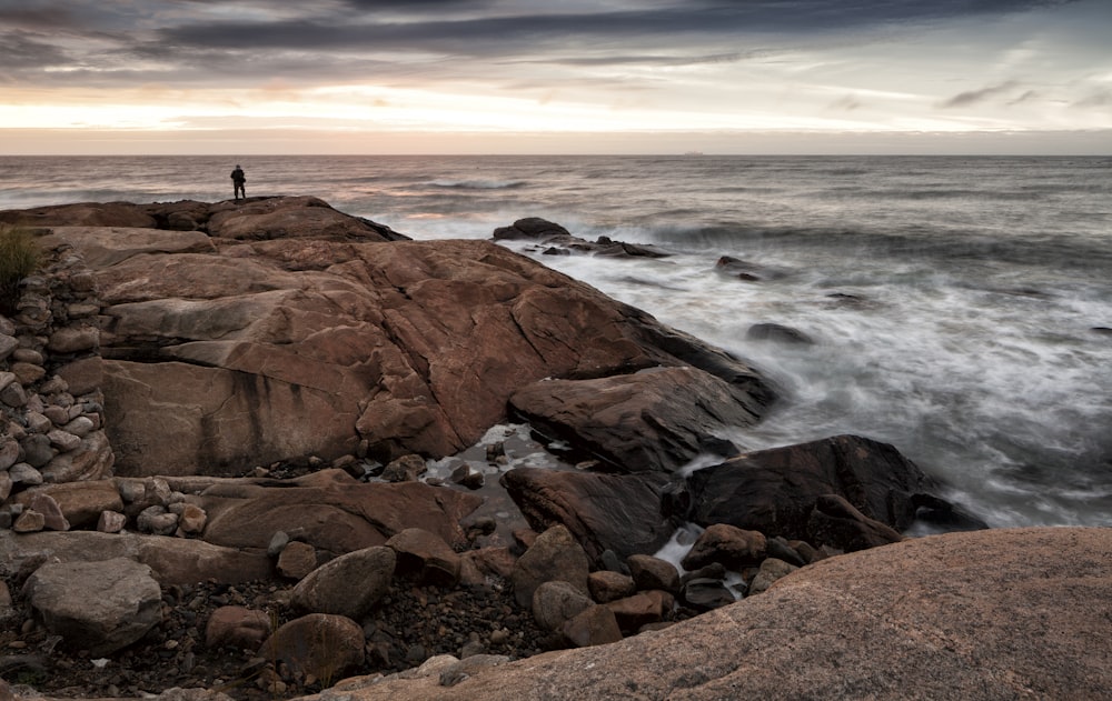 person standing on rock formation near sea during daytime