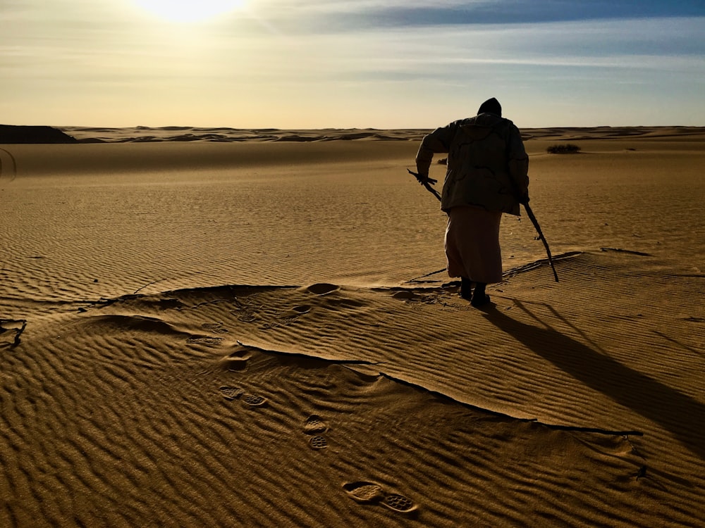 uomo in camicia nera e pantaloni neri in piedi su sabbia marrone durante il giorno