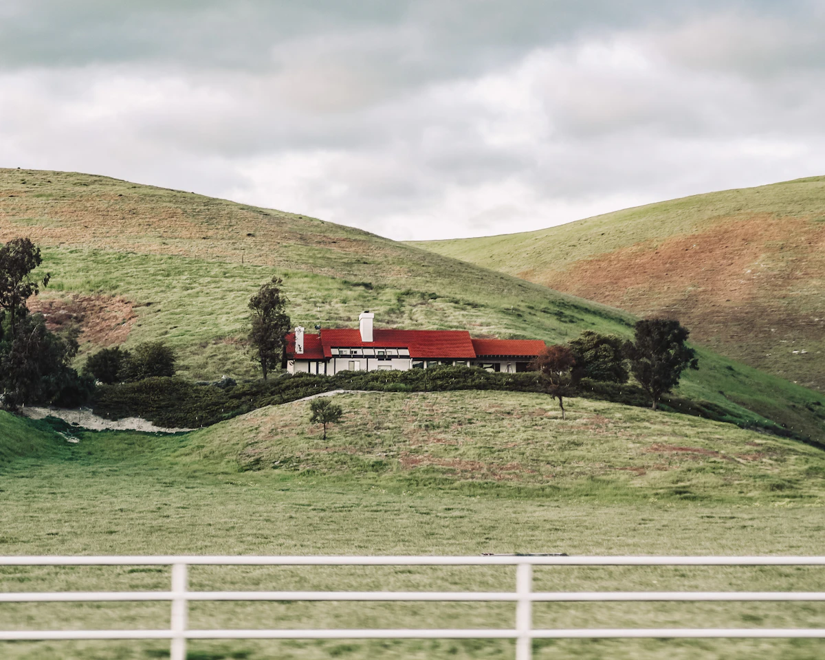 Red and white farmhouse on a green hillside near a mountain