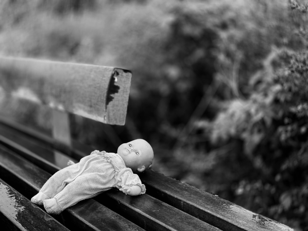 grayscale photo of baby doll on wooden bench