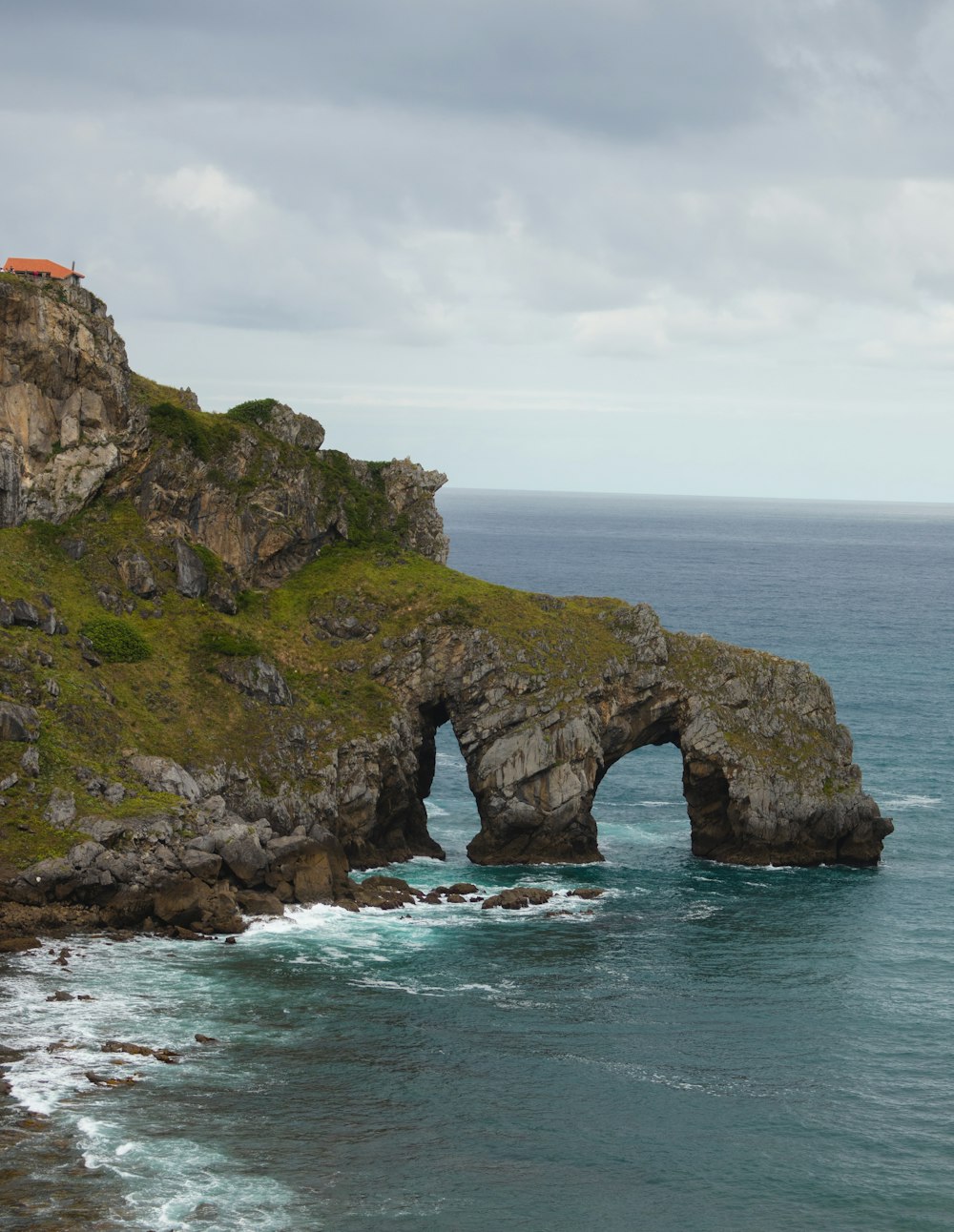 brown and green rock formation on sea under white clouds during daytime