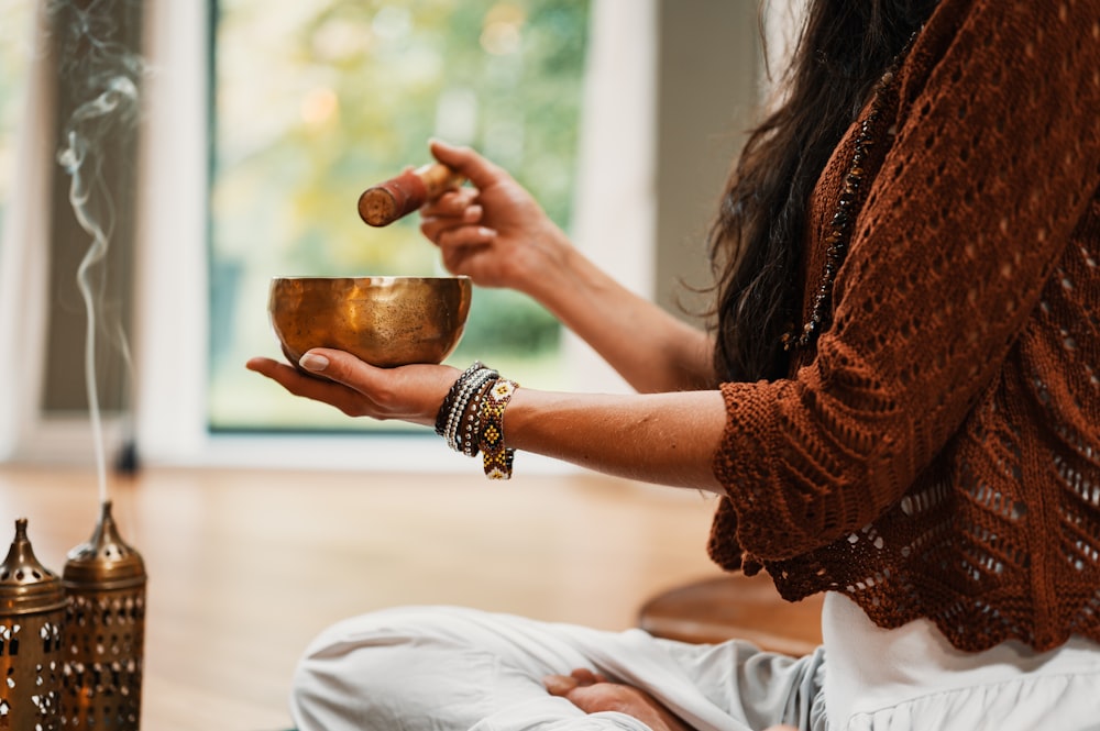 woman in brown knit sweater holding a tibetan bowl