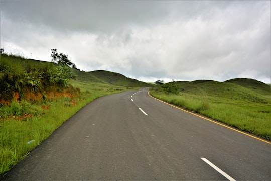 gray concrete road between green grass field under gray sky in Jowai India