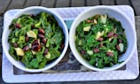 Two bowls filled with a green leafy salad composed of chopped greens, red kidney beans, and slices of garlic. The bowls are white and placed on a rectangular tray.