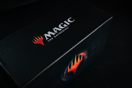 A black box featuring the bold logo and text 'Magic: The Gathering' in white, accompanied by a striking red and orange flame-like emblem.