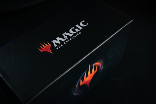A black box featuring the bold logo and text 'Magic: The Gathering' in white, accompanied by a striking red and orange flame-like emblem.