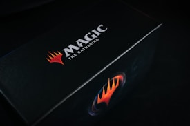 A black box featuring the bold logo and text 'Magic: The Gathering' in white, accompanied by a striking red and orange flame-like emblem.