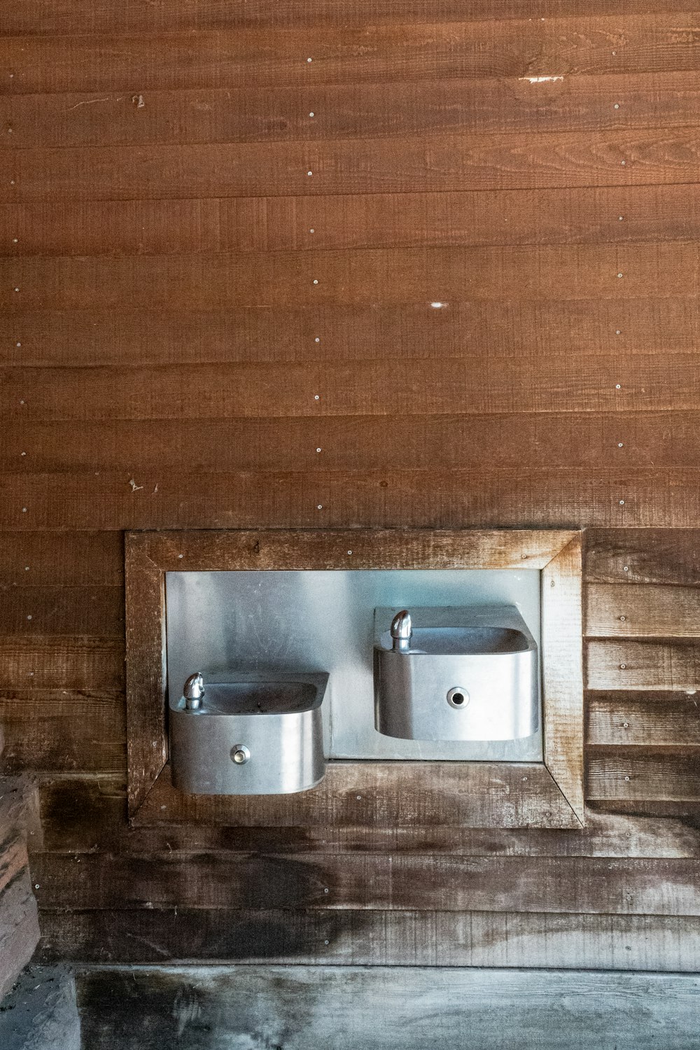 dois dispensadores de sabão de metal montados em uma parede de madeira