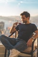 man in black crew neck t-shirt and blue denim jeans sitting on chair