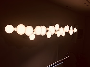 A series of round, white light bulbs arranged in a linear pattern on a dark background. The lights are glowing, casting a warm, atmospheric illumination.