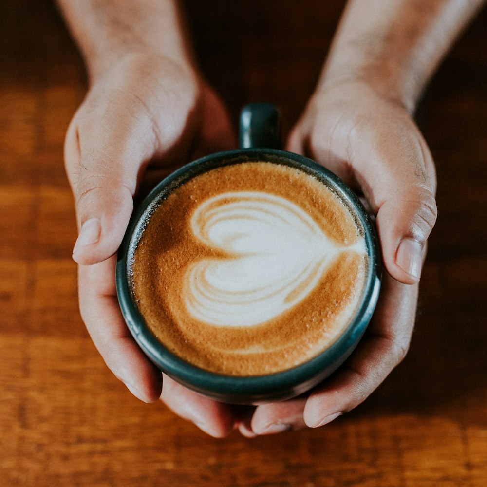 person holding black ceramic mug with brown and white liquid