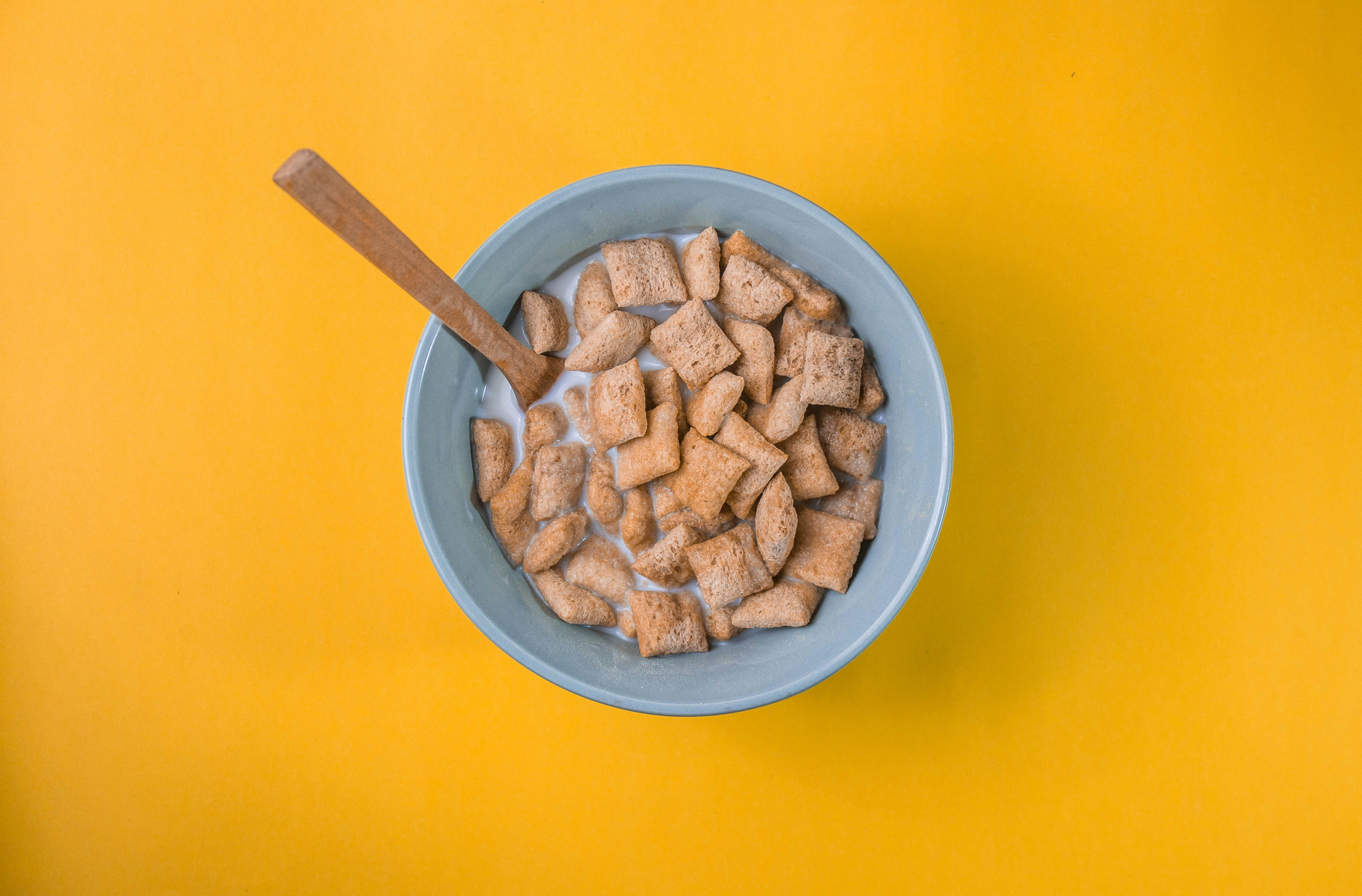 Square blocks of cereal in milk in a blue bowl against a mustard yellow background.