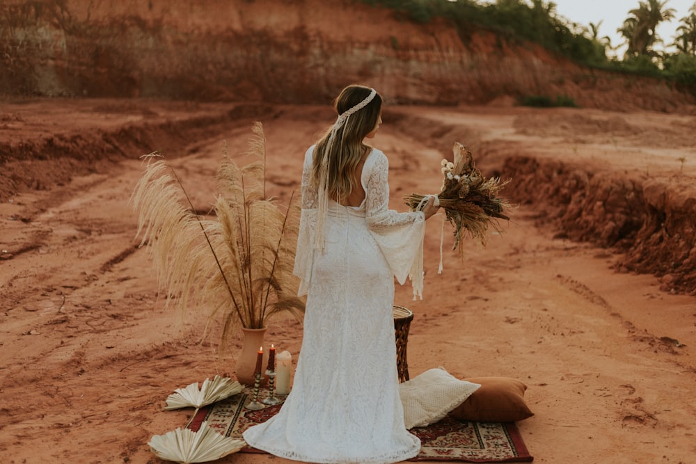 donna in abito da sposa bianco che si siede su sabbia marrone durante il giorno