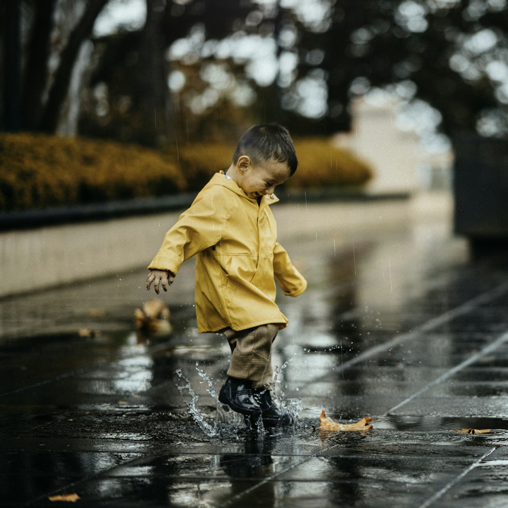 child in yellow hoodie walking on wet road during daytime