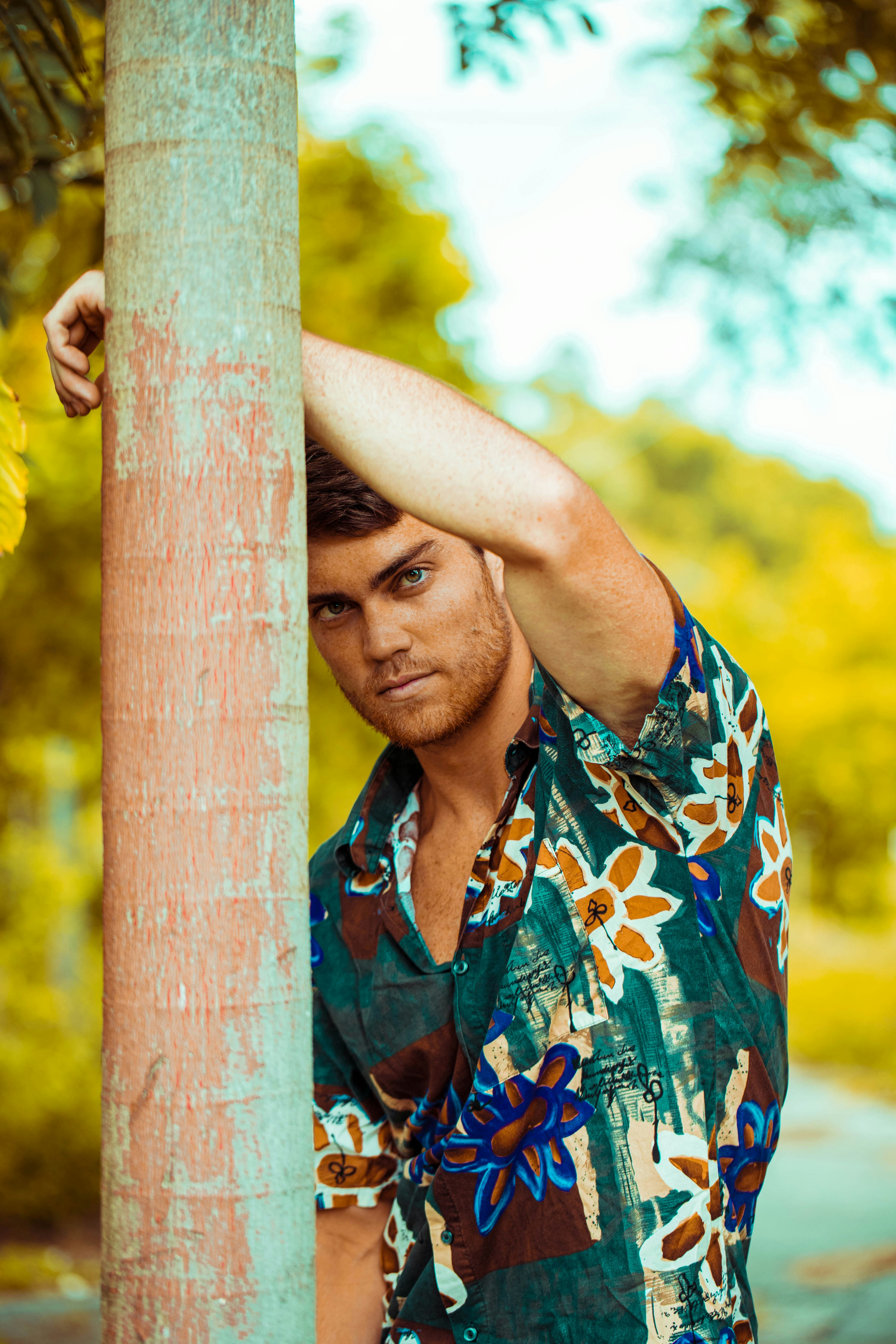 woman in green and brown floral shirt holding on brown wooden post during daytime