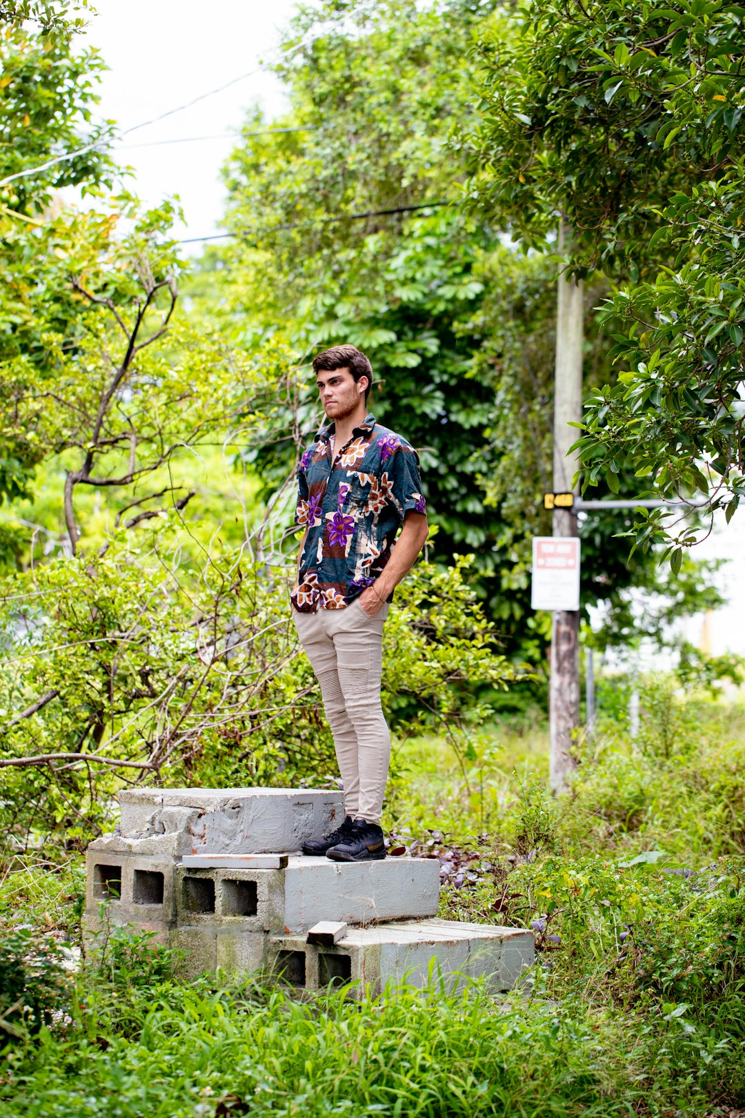 woman in blue and green floral shirt and brown pants standing on gray concrete bench during