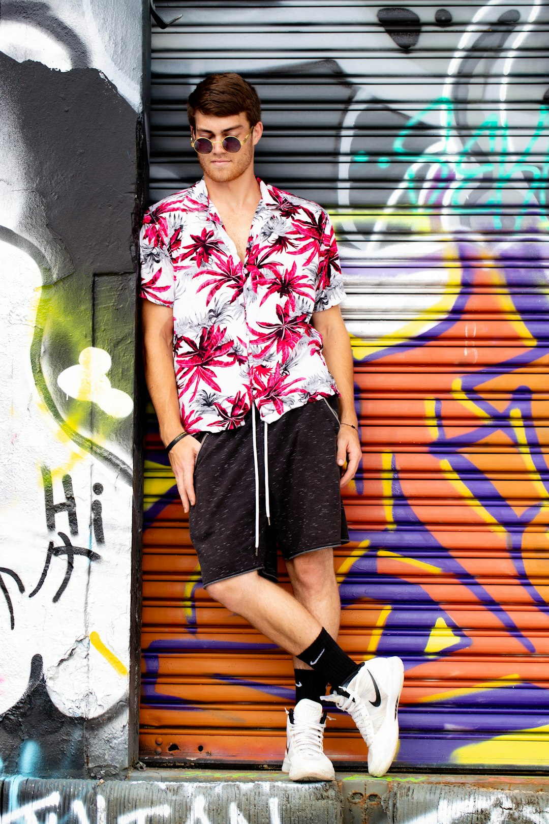 woman in white red and blue floral button up shirt and black shorts standing beside wall