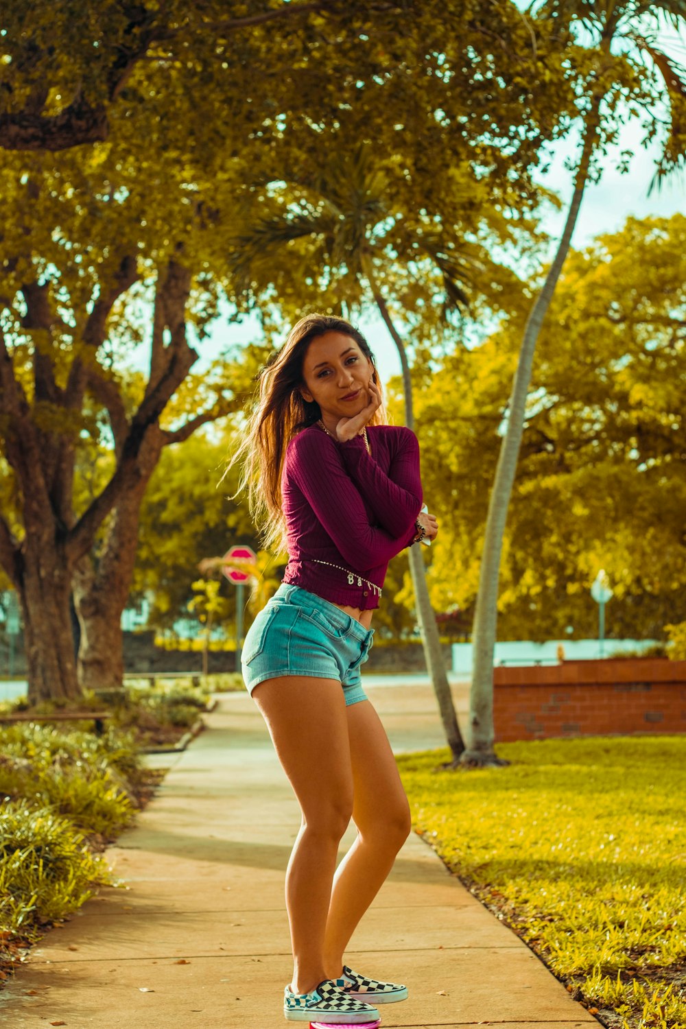 woman in purple long sleeve shirt and blue denim shorts standing on pathway during daytime