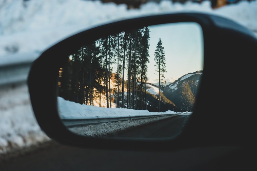 car side mirror showing snow covered trees