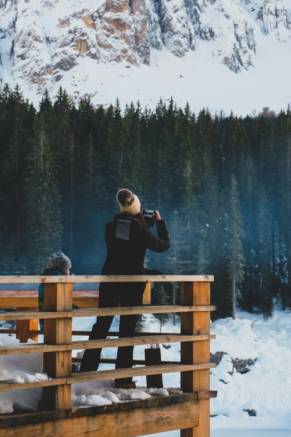 woman in black jacket and black pants sitting on brown wooden fence during daytime