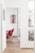 A bright, modern interior with white walls and wooden flooring. Red chairs with metal legs are aligned in the room. There is a colorful abstract painting on the wall and a few potted plants are visible through a large window, adding greenery to the space.