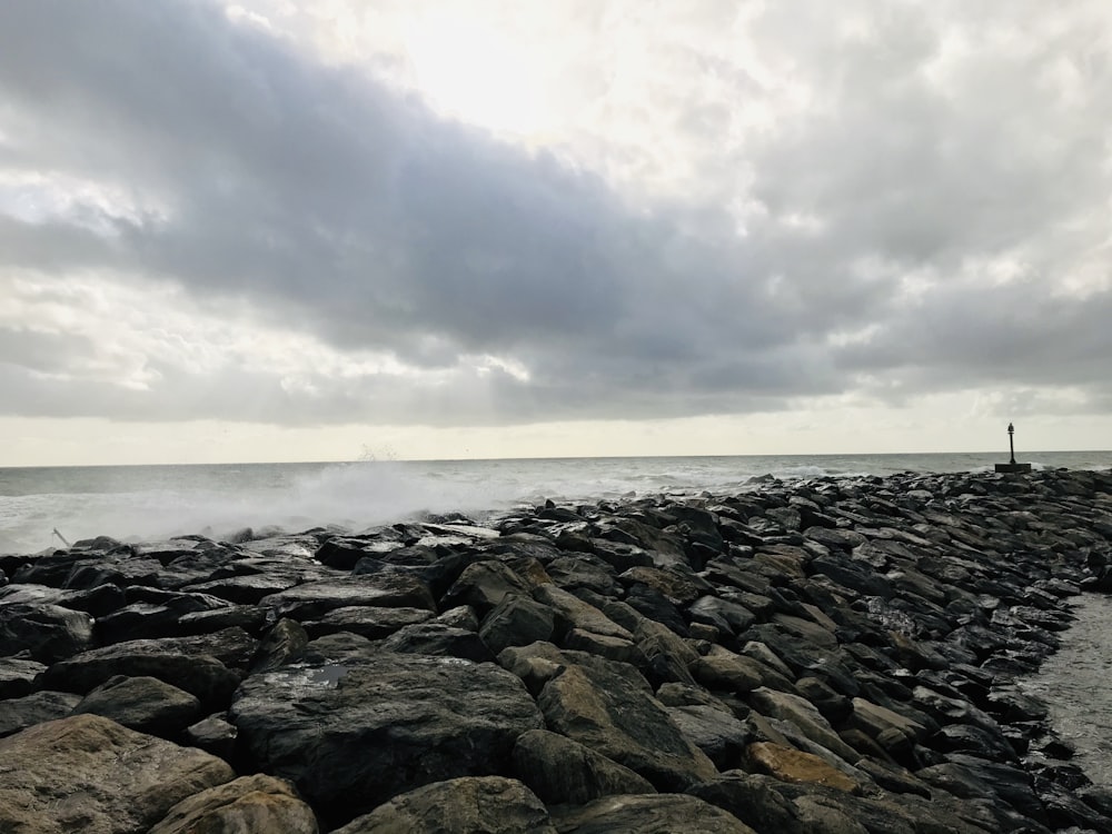 gray rocks near body of water under white clouds during daytime